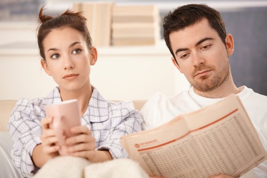 Young couple in bed man reading woman bored