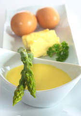 Asparagus lying on a bowl full of Hollandaise sauce
