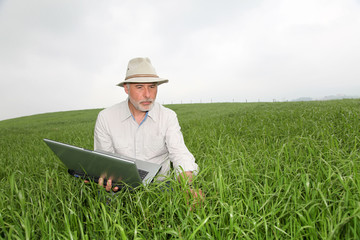 Farmer examining crop with laptop computer