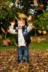 Happy red haired boy playing in autumn leaves in park