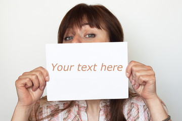 Young cute girl hiding behind a sheet of paper for text