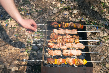 Man's hand turns the skewer with a barbecue on the grill