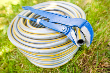 Blue metall spanner and plastic hose on green grass
