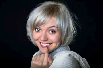 The smiling girl holds a finger at  mouth