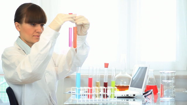 Scientist examines test tubes and writing results on laptop