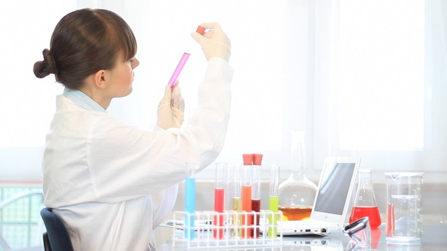 Scientist examines test tube and writing results on laptop