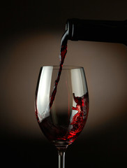 Naklejka na ściany i meble Red wine pouring into glass over dark background