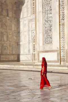 Woman in red sari/saree walking past Taj Mahal.