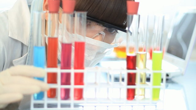 scientist examine test tubes and writing results on laptop