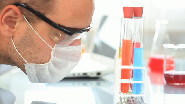 scientist looking at test tubes and writing results on laptop