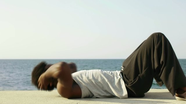 african man exercising abs near the sea