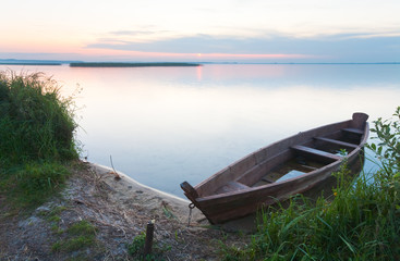 Obraz premium Sunset with old flooding boat on summer lake shore