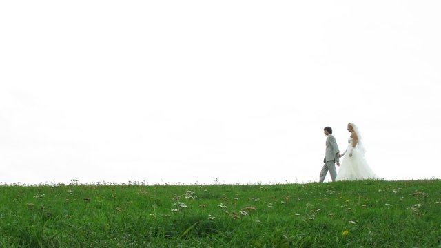 Newlywed pair walks on grass in front of cloudy white sky