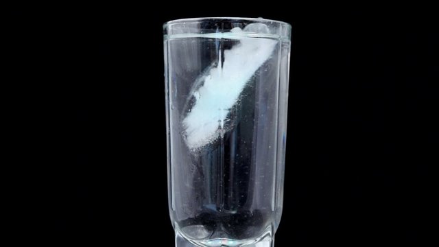 glass with water and ice rotating in LED illumination on black