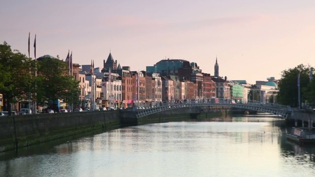 People are crossing Ha'penny Bridge, cars moving along bank