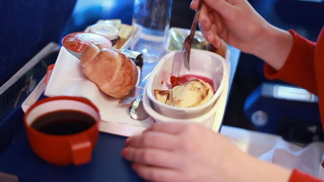 tray with food on airplane, woman's hand takes bit of meat fork