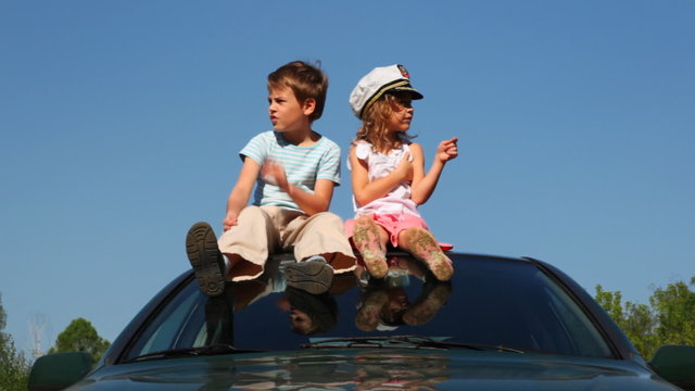boy and girl in captain's cap sit on roof of car