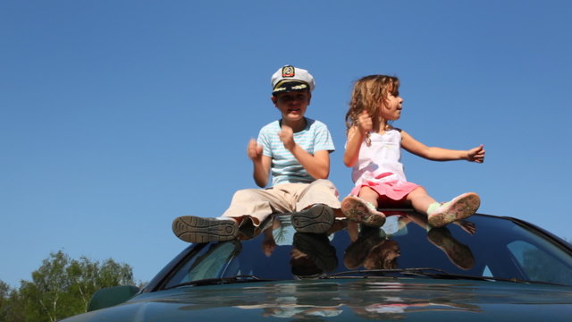 boy in captain's cap and little sister sit on car