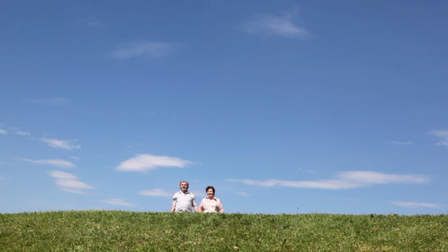 mature couple goes lively talking by grass against sky