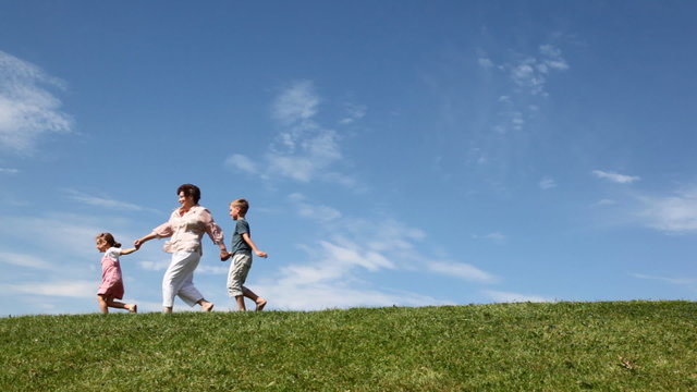boy and girl with grandmother holding hands run down by grass