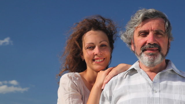 senior and daughter leaning hands on his shoulder, against sky