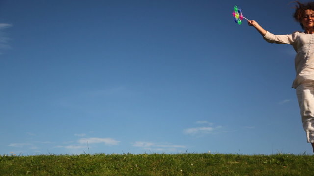 woman runs and turns on grass holding oy windmill against sky
