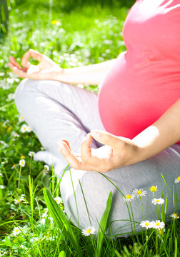 Beautiful pregnant woman relaxing in the park, yoga pose
