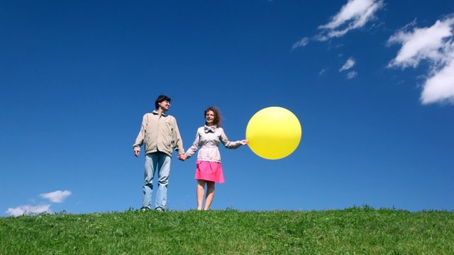 man with woman holding hands with yellow bubble stand on hill
