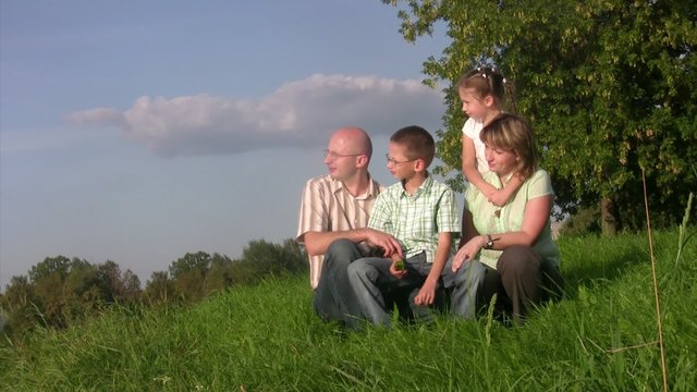 Family sits in grass and looks afar. Summer day.