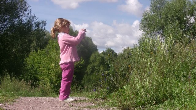 Little girl photographs in summer park, sunny day.