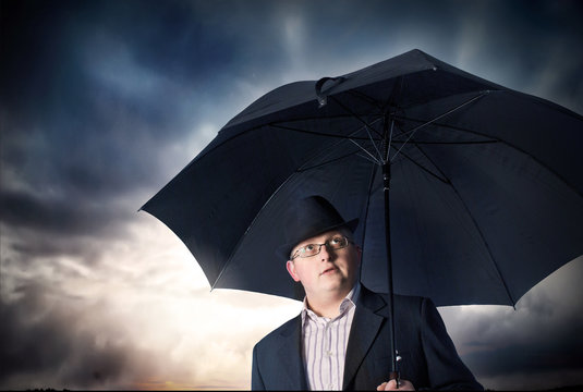 Businessman with umbrella and storm clouds background