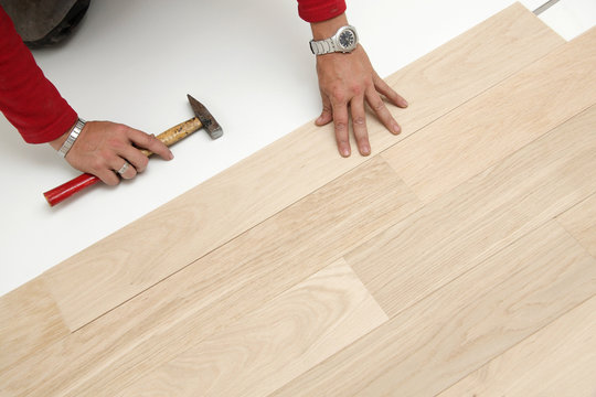 mains posant parquet en ch&ecirc;ne semi-massif avec marteau