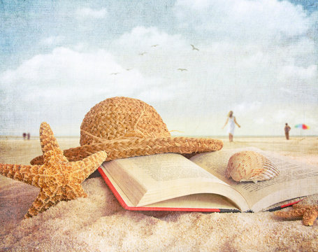 Straw hat , book and seashells in the sand