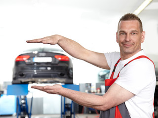 Car mechanic in a garage holding his hands over and among a car