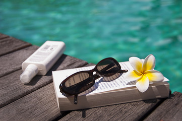Livre, lunettes et crème solaire à la piscine - obrazy, fototapety, plakaty