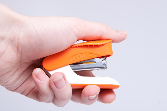 Woman's hand with orange Stapler isolated on grey background