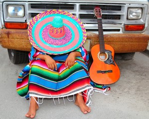 Man wearing sombrero and poncho resting in front of a truck