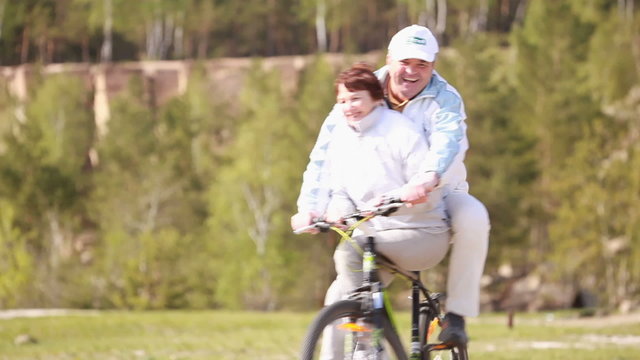 Two senior people riding a bike