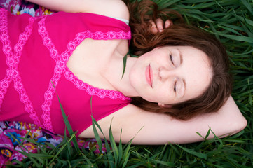 Obraz na płótnie Canvas Redhead woman lying on the green grass