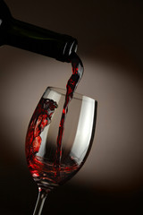 Red wine pouring in glass over dark background