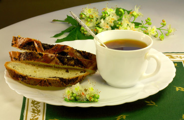 A cup of tea, a white bread with a poppy and chestnut tree flowe