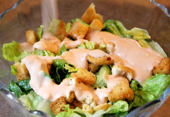 Salad dressing being poured on fresh lettuce and croutons
