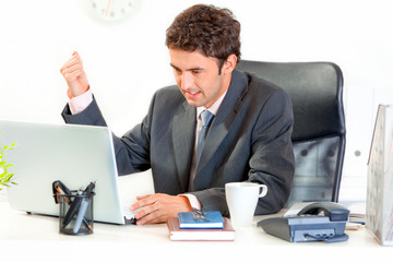 Businessman sitting at desk and brandishing fist on laptop.