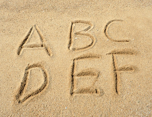 alphabet letters handwritten in sand on beach