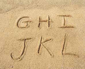 alphabet letters handwritten in sand on beach