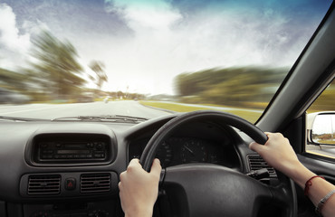 Hands on steering wheel of a car and motion blurred asphalt road and sky