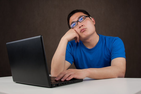 Bored And Tired Young Asian Man Working With His Computer