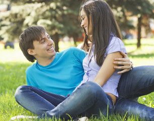 Romantic young couple sitting together at park on the grass and
