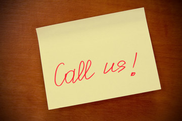 wooden board  with yellow  sticky note "call us" .