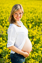 Naklejka na ściany i meble Pregnant woman sitting on green field